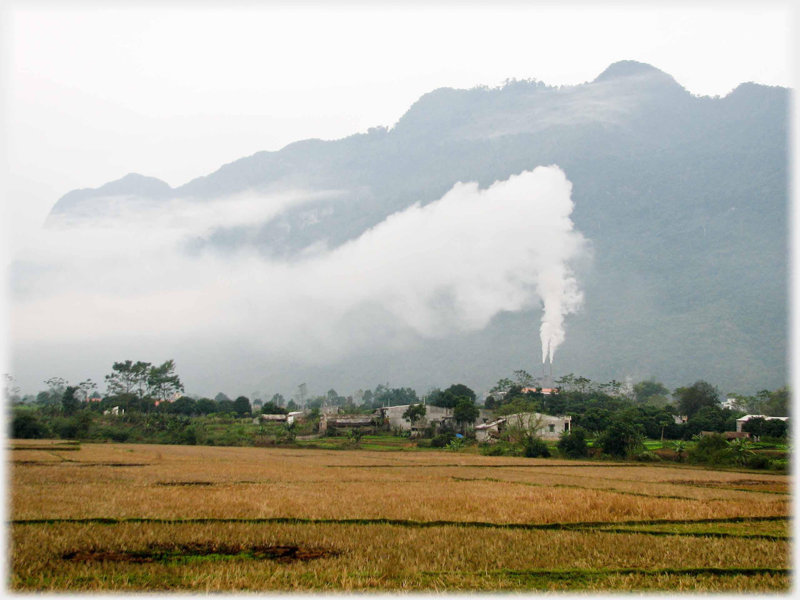 Backdrop of hills with two chimnies issuing large plumes of smoke.