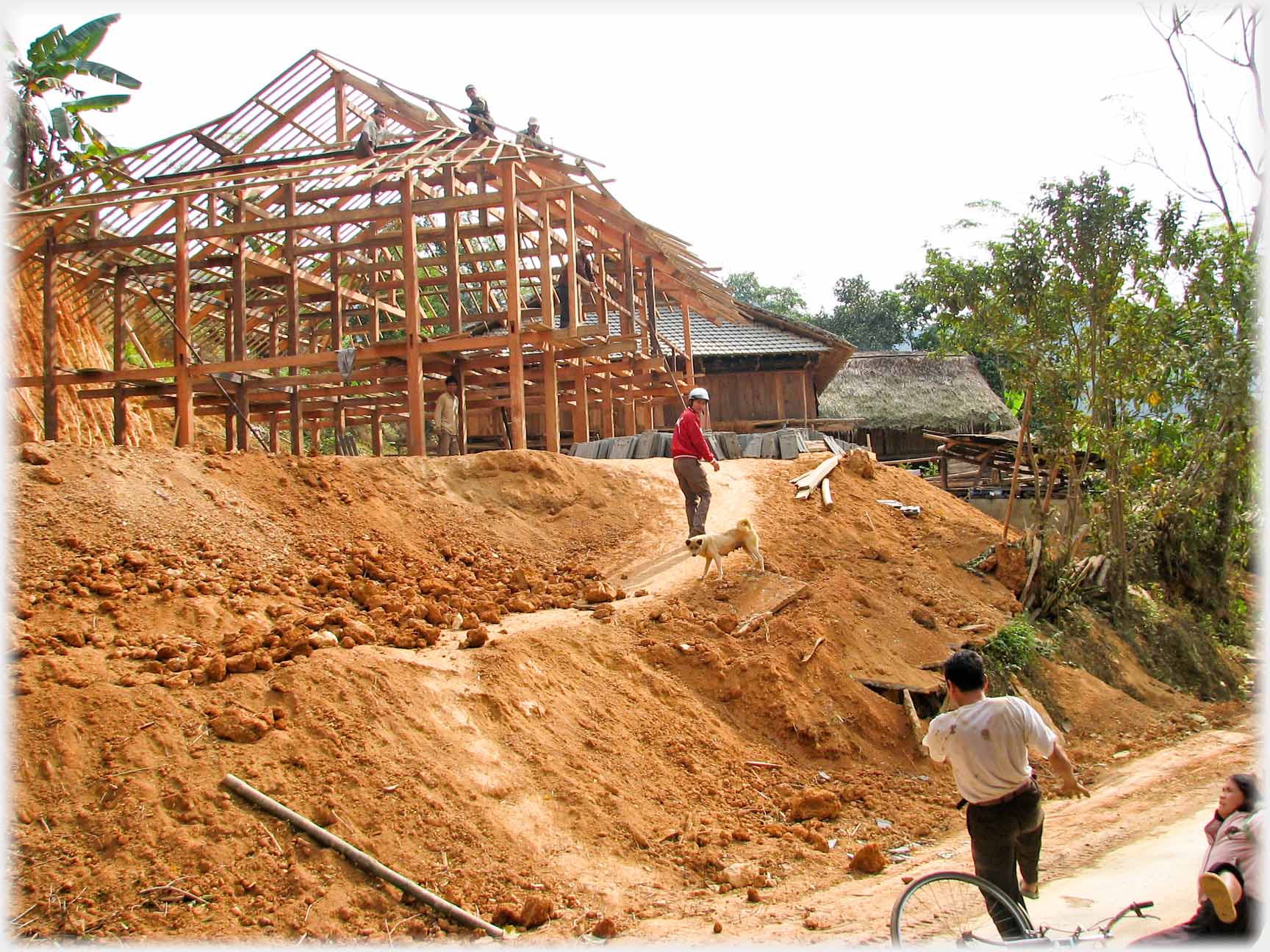 Wooden skeleton of stilt house on bank, Han turning while walking to it, builders on roof looking at two people just in corner of photo, one falling the other legs in air.