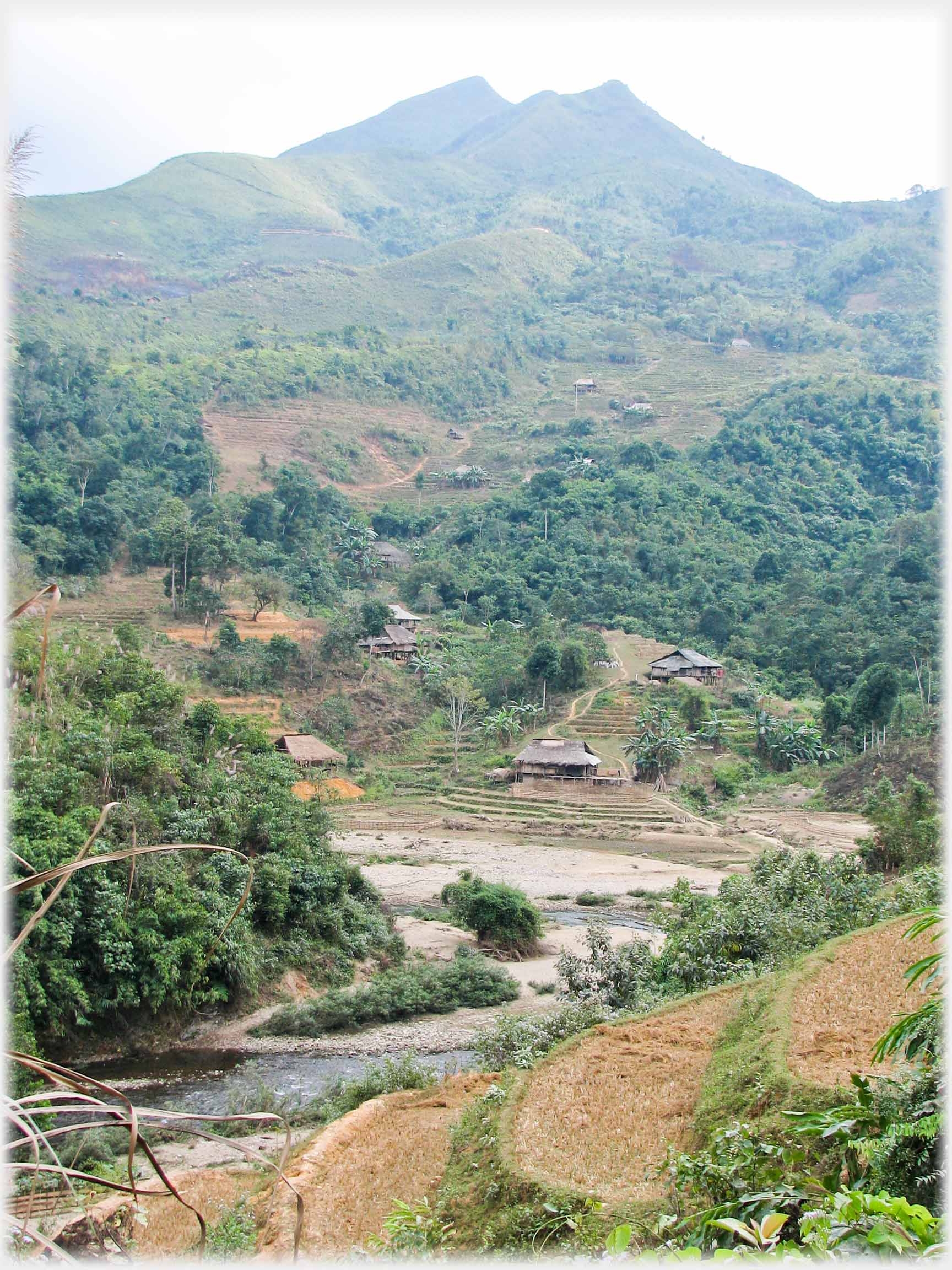 Peaked background hill with river and village in foreground.