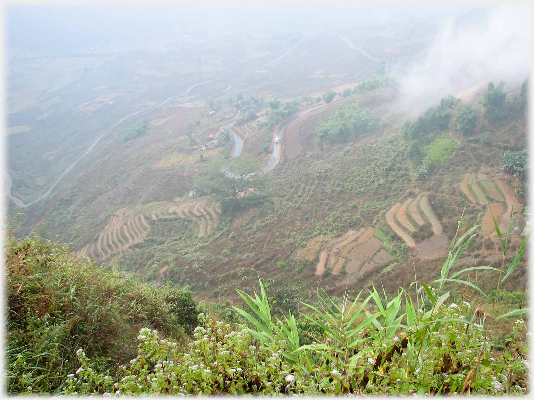 Looking down steep terraced hillside with road looping away down the hill, slight cloud.