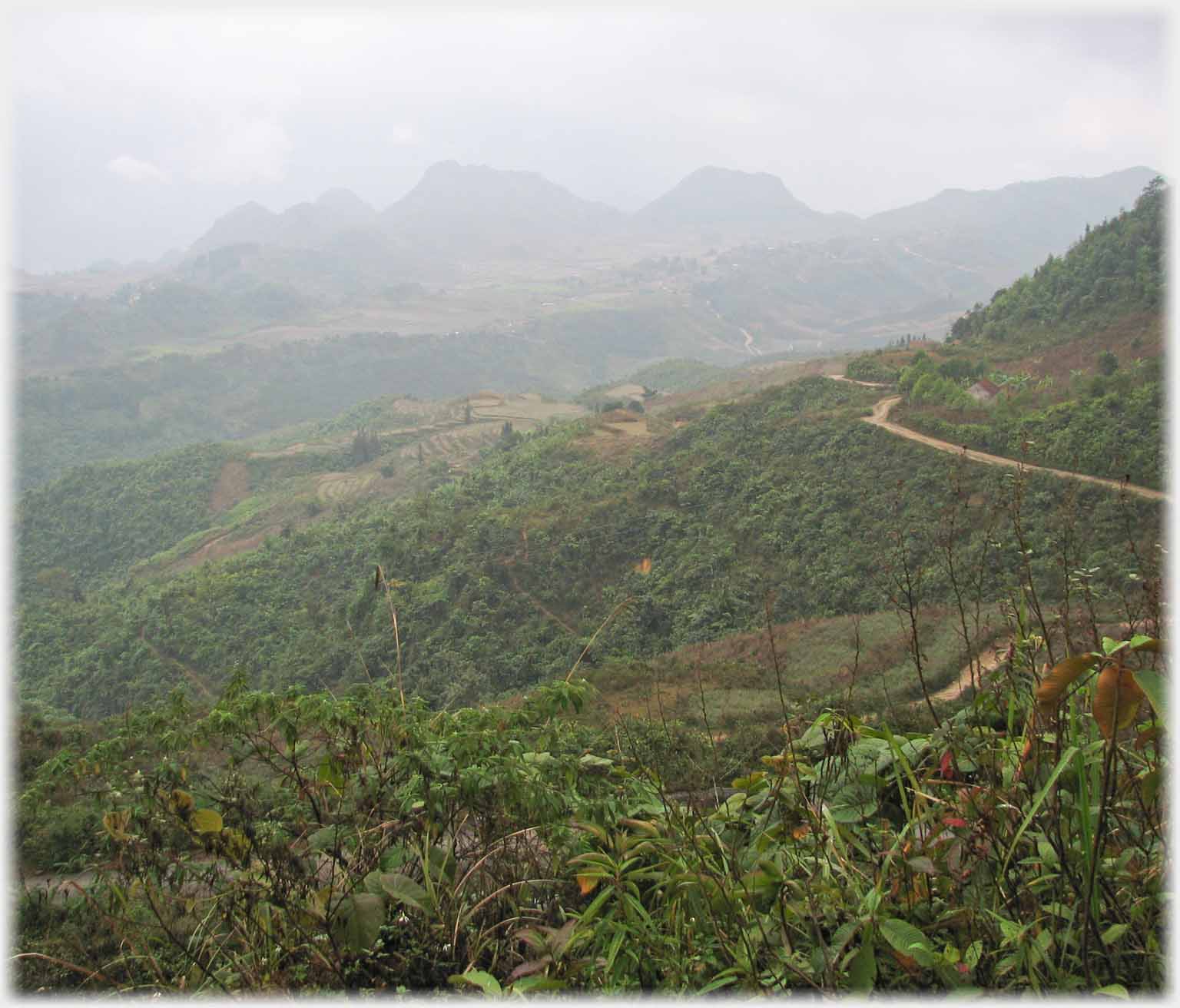 Sloping scrub covered ground with road and distant hills.