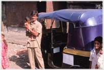 Auto driver standing beside his machine holding infant.