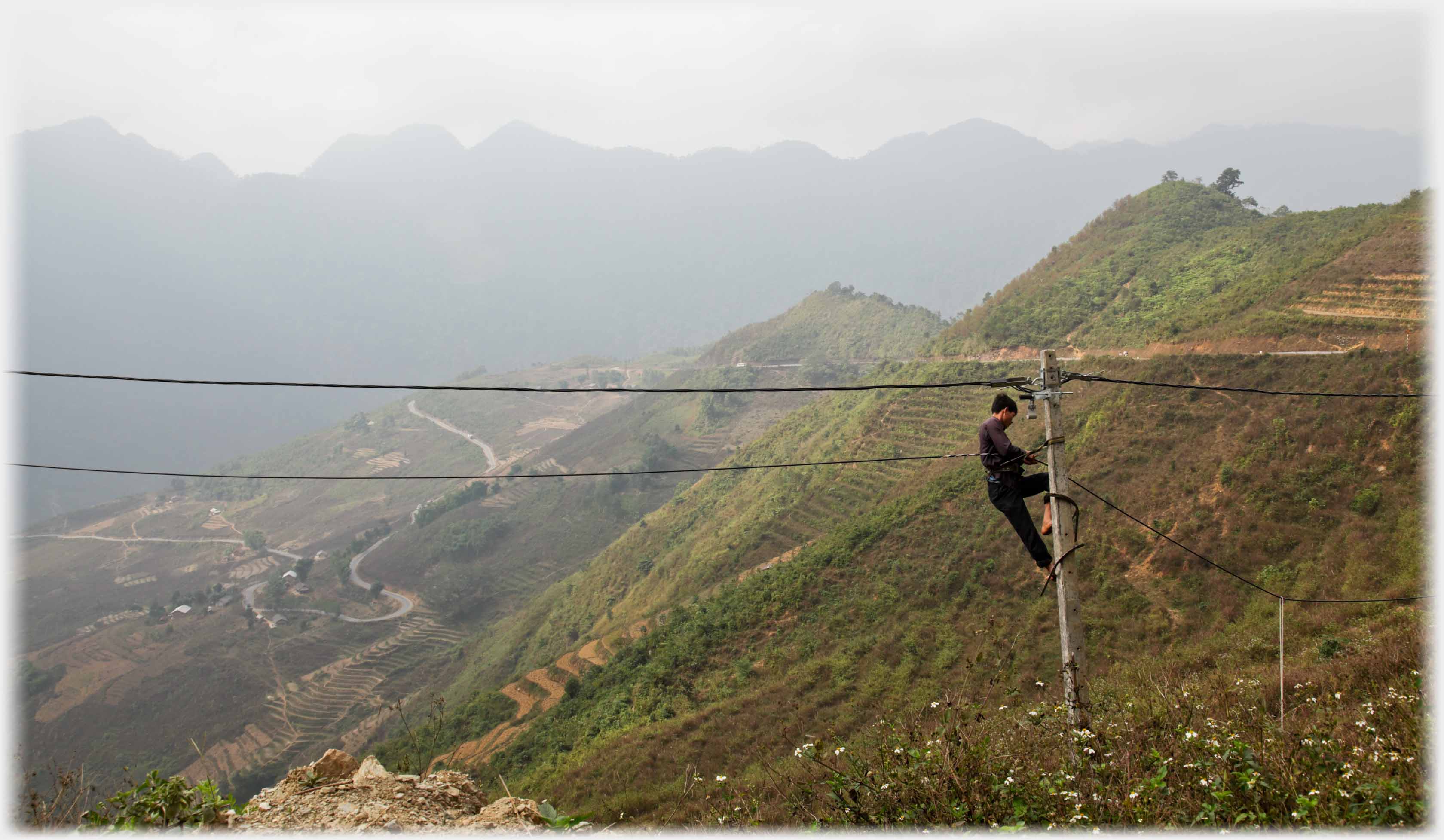 Man up pylon with extensive hillside and mountains beyond.