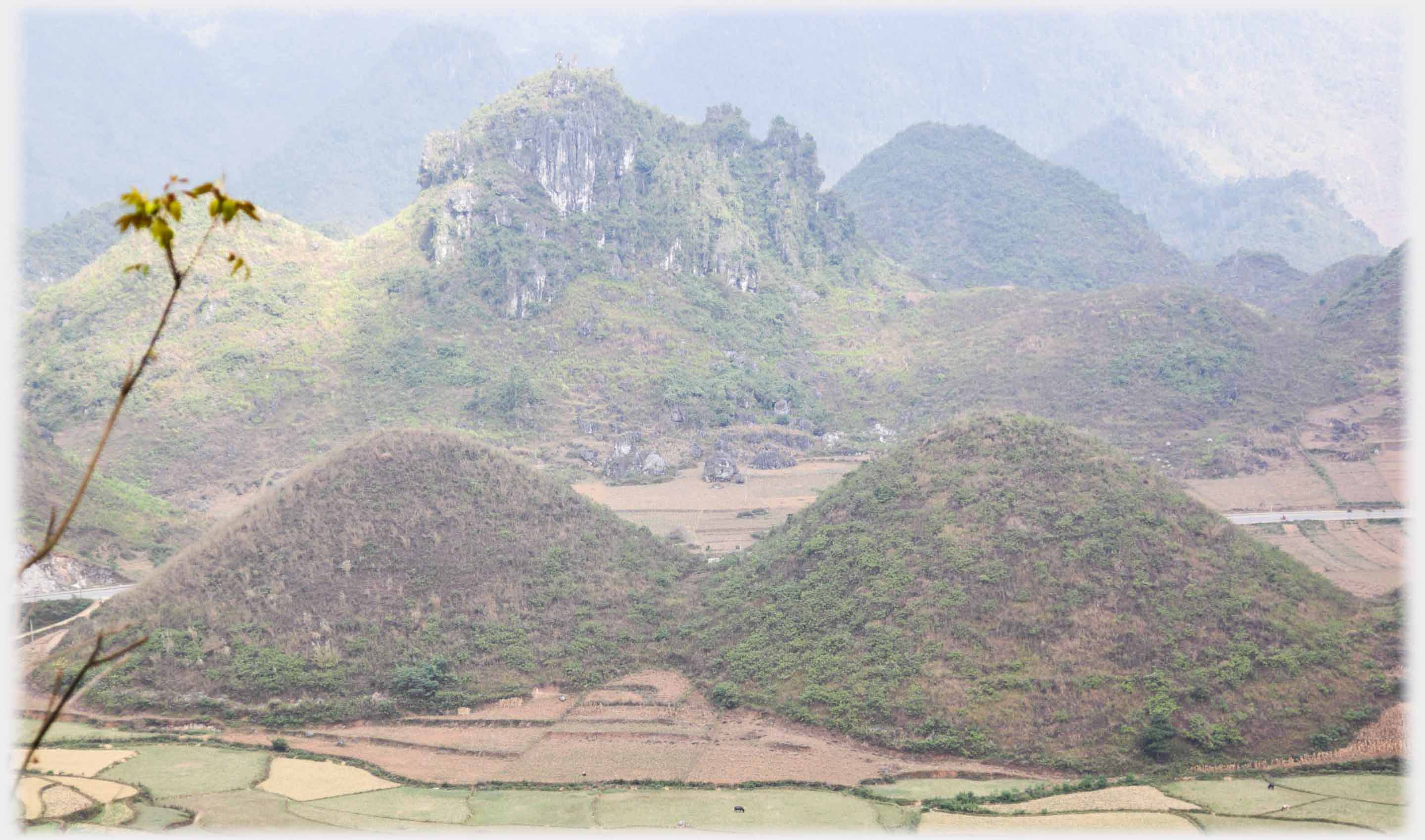 Pair of equqlly breast shaped small hills in front of cragy hills.