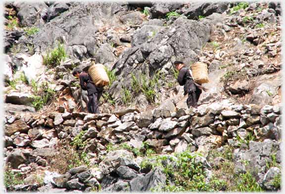 Two men walking between rocks with back-baskets.