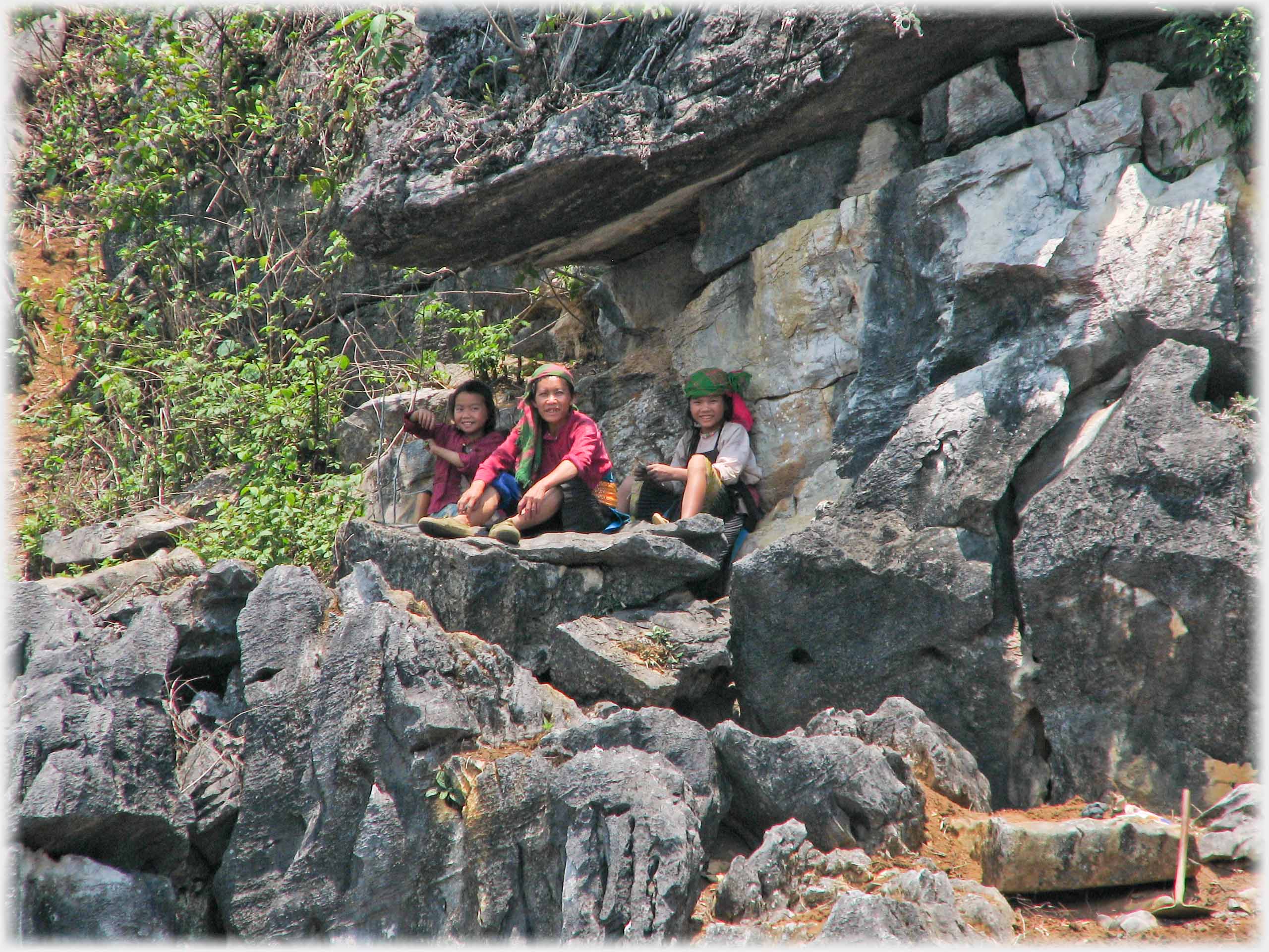 Three women on ledge under overhanging rock, shovel to side.