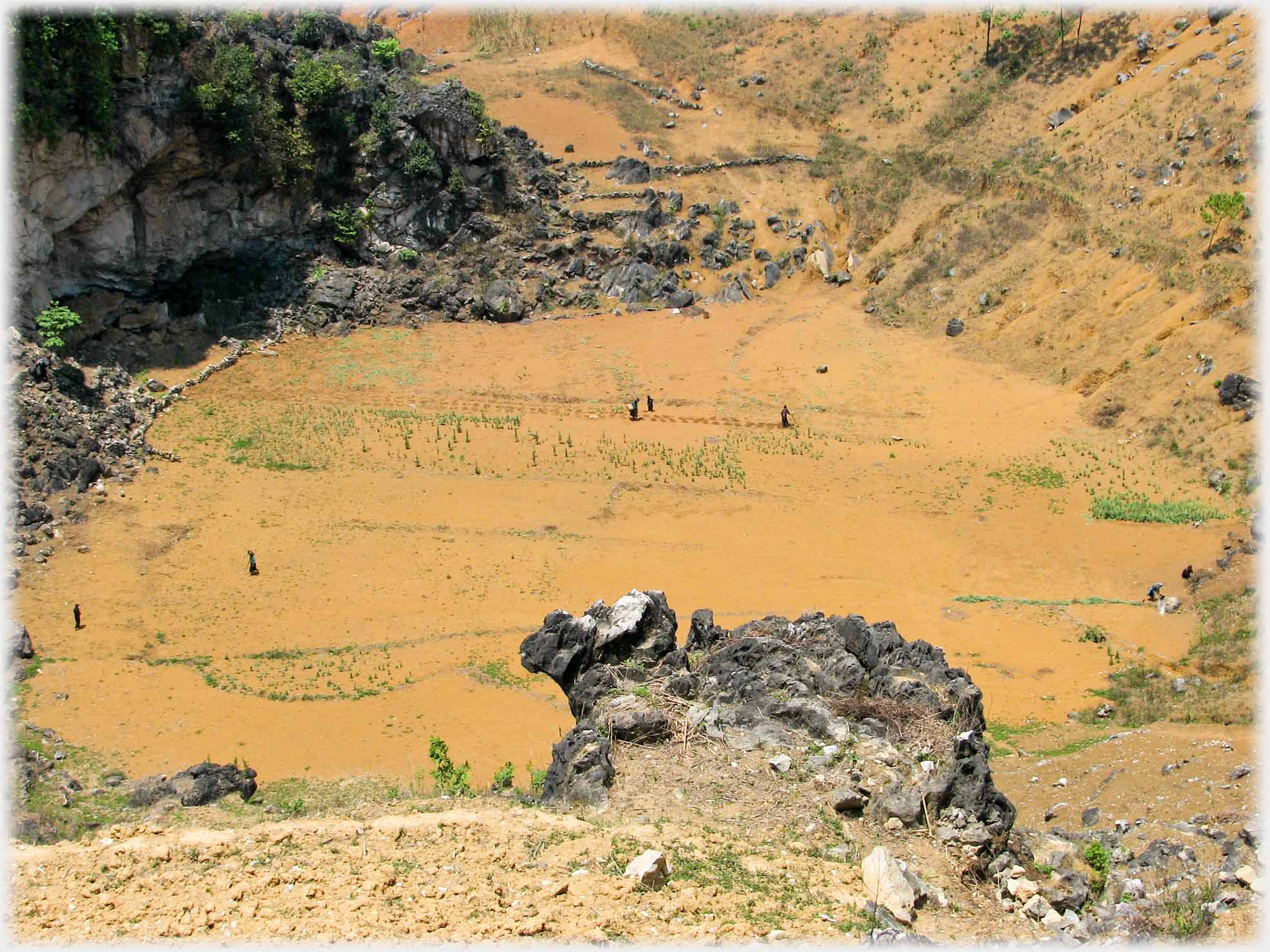 Looking down at a flat valley bottom of oche soil, dotted with figures.
