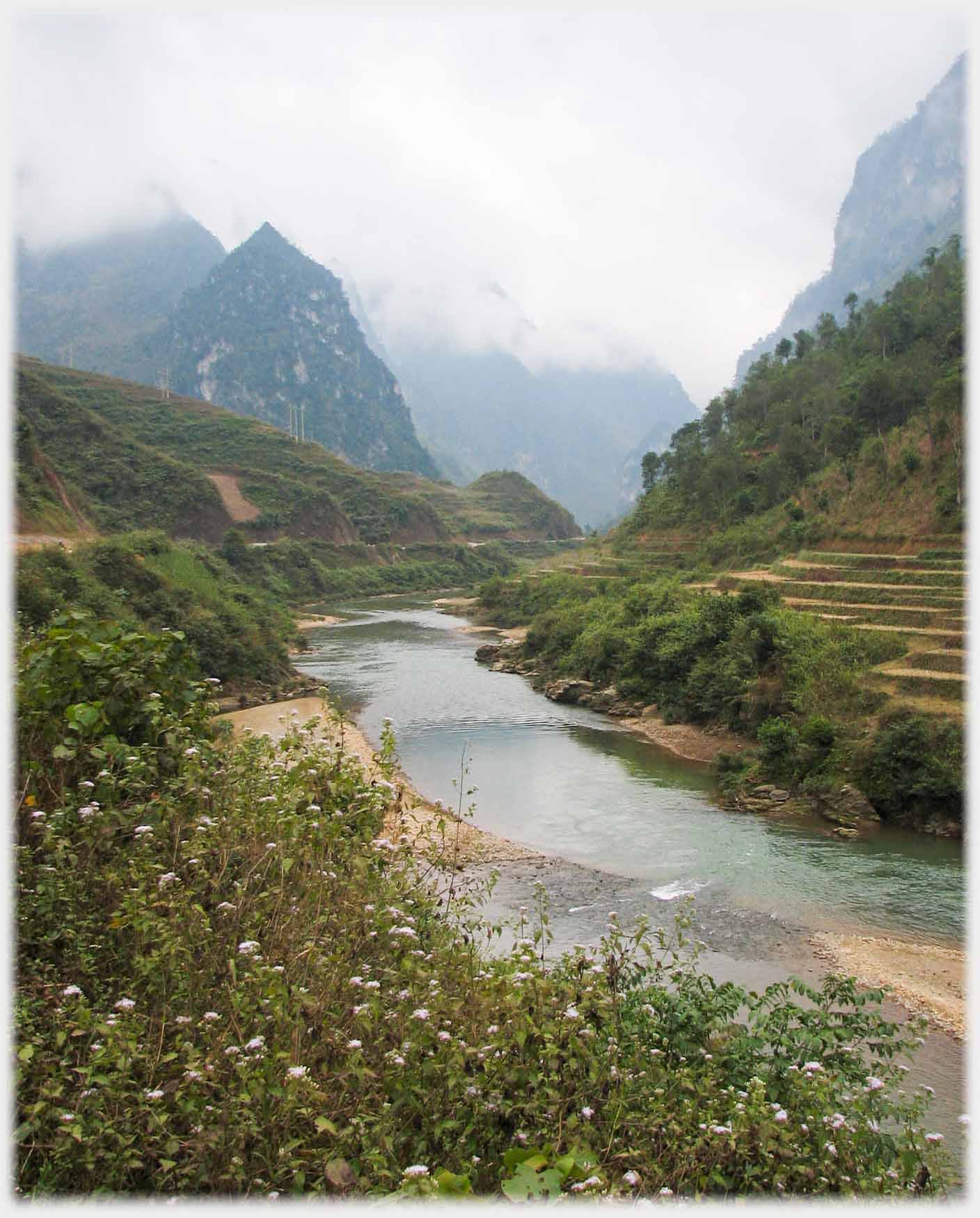 River in valley with steep hillsides and mist down on the hills.