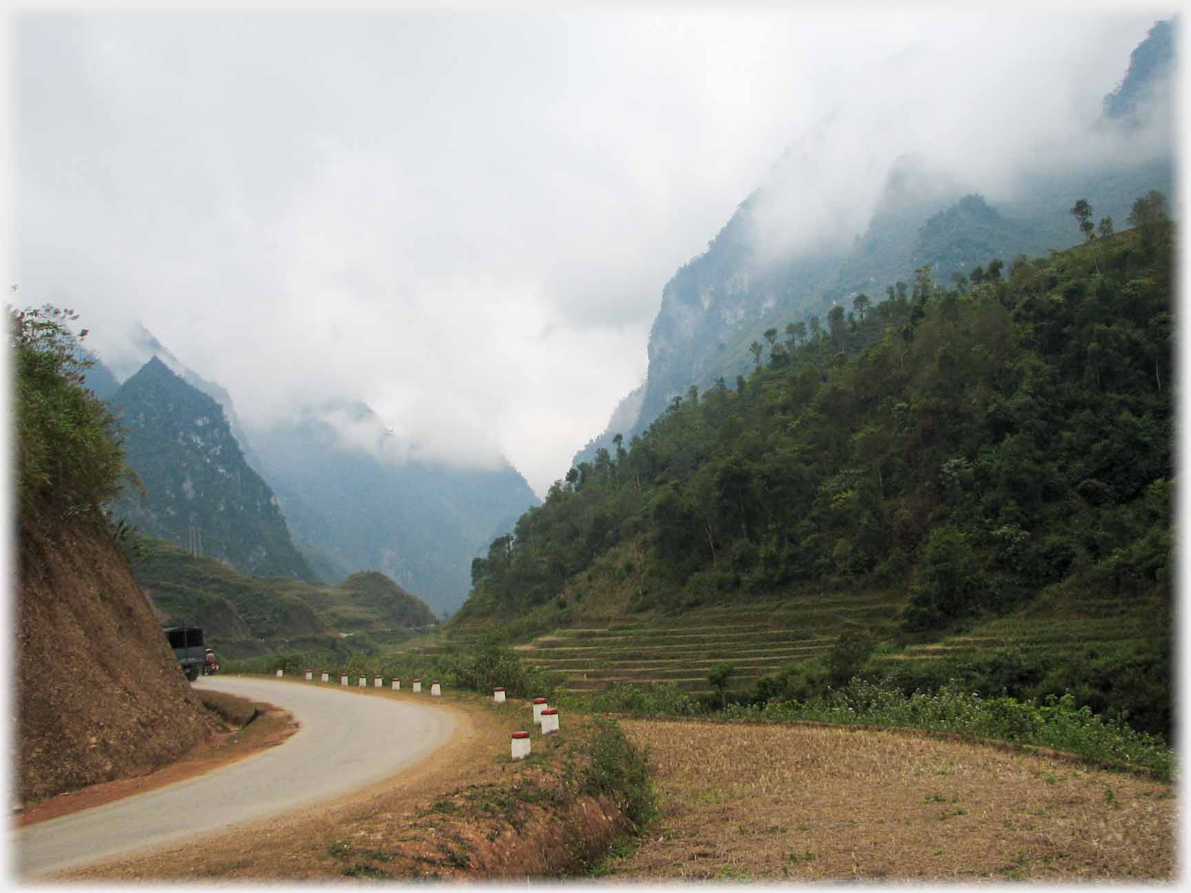 Road curving away through valley with clouds around hill tops.