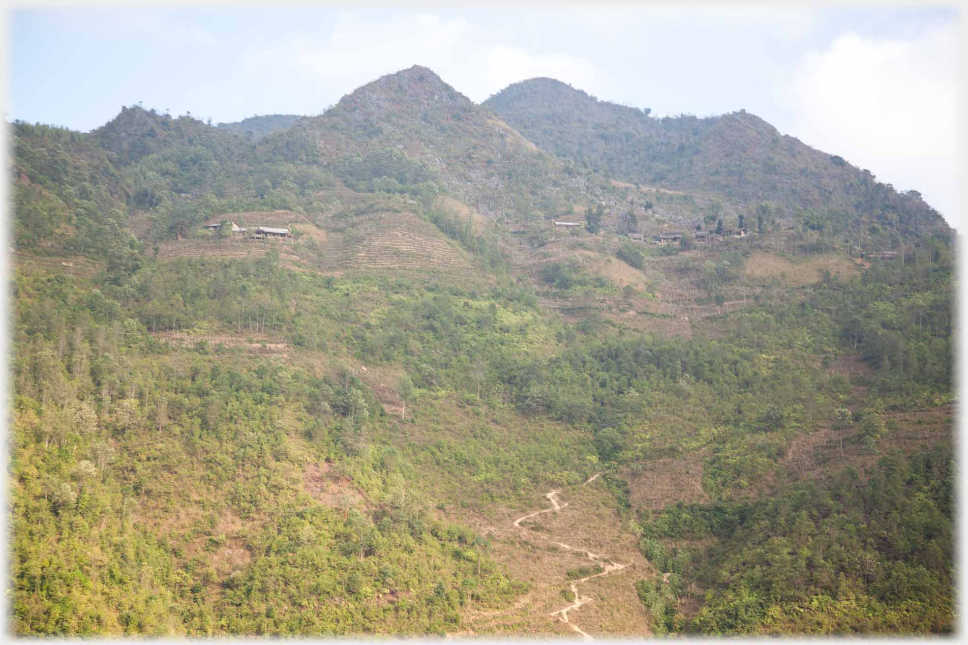 View looking up from a valley houses dotted and a winding path ahead.