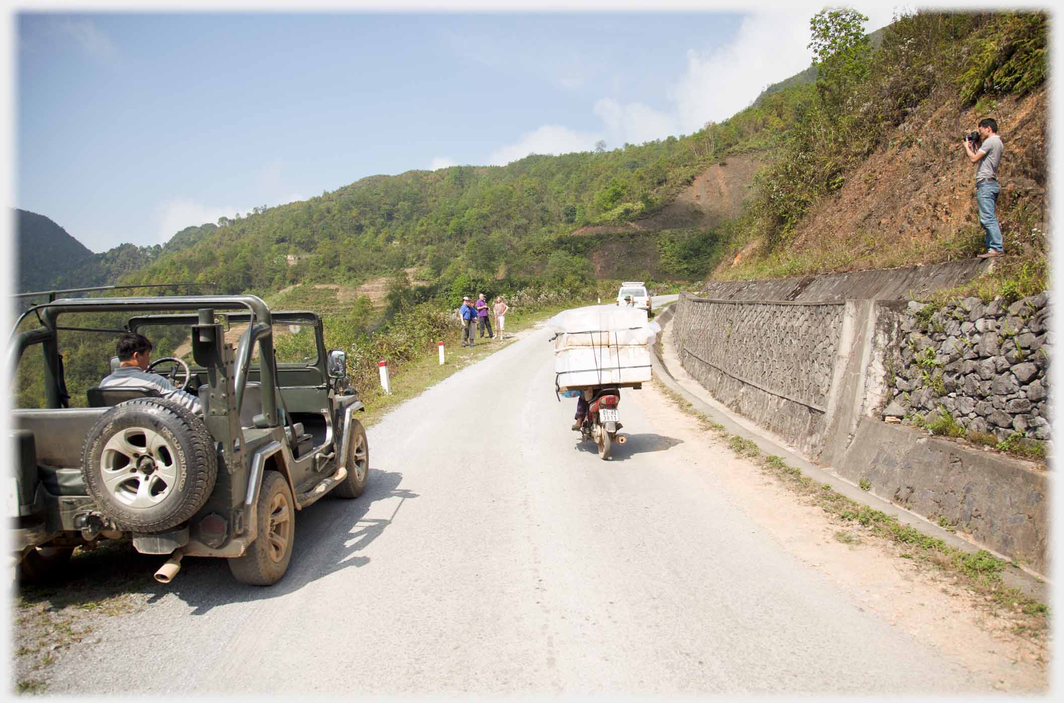 Jeep parked at roadside, passing motorbike, Han up bank photographing visitors down the road.