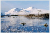 Snow covered hills beyond ice covered loch.
