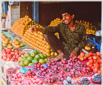 Man sitting amongst piles of fruit.