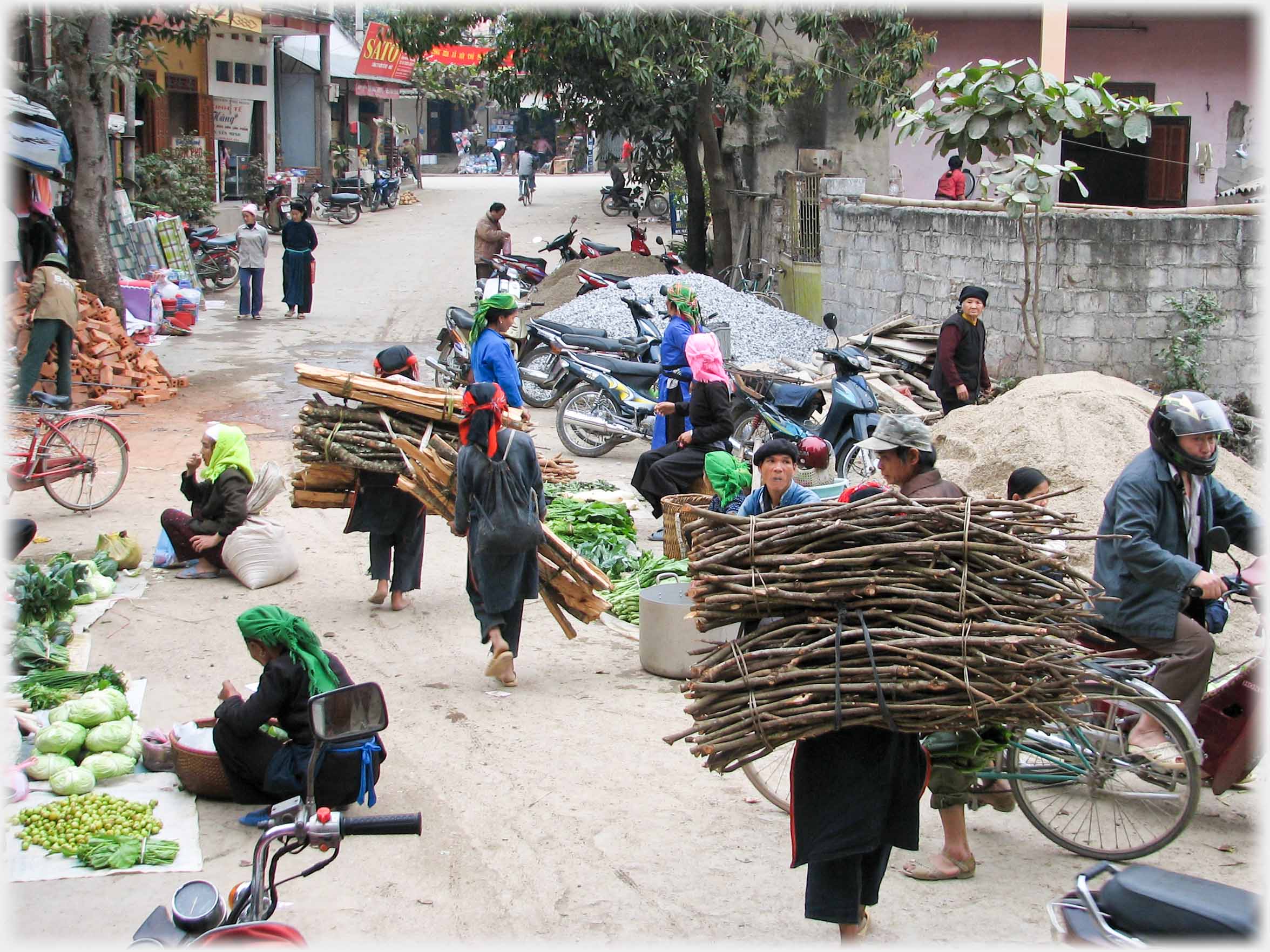 Three women carrying bundles of wood walking down the street.