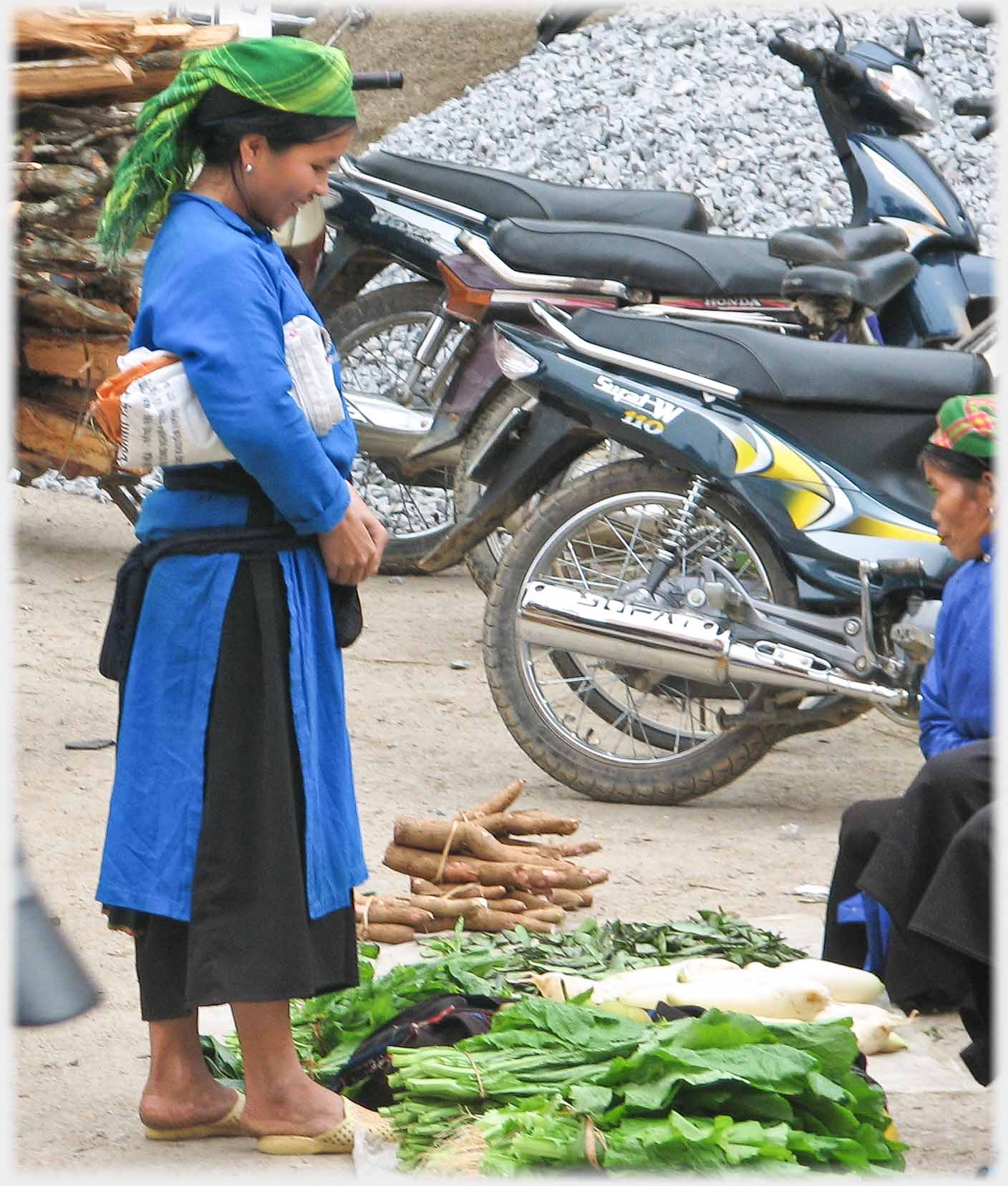 Woman in long blue overshirt looking at vegetables.