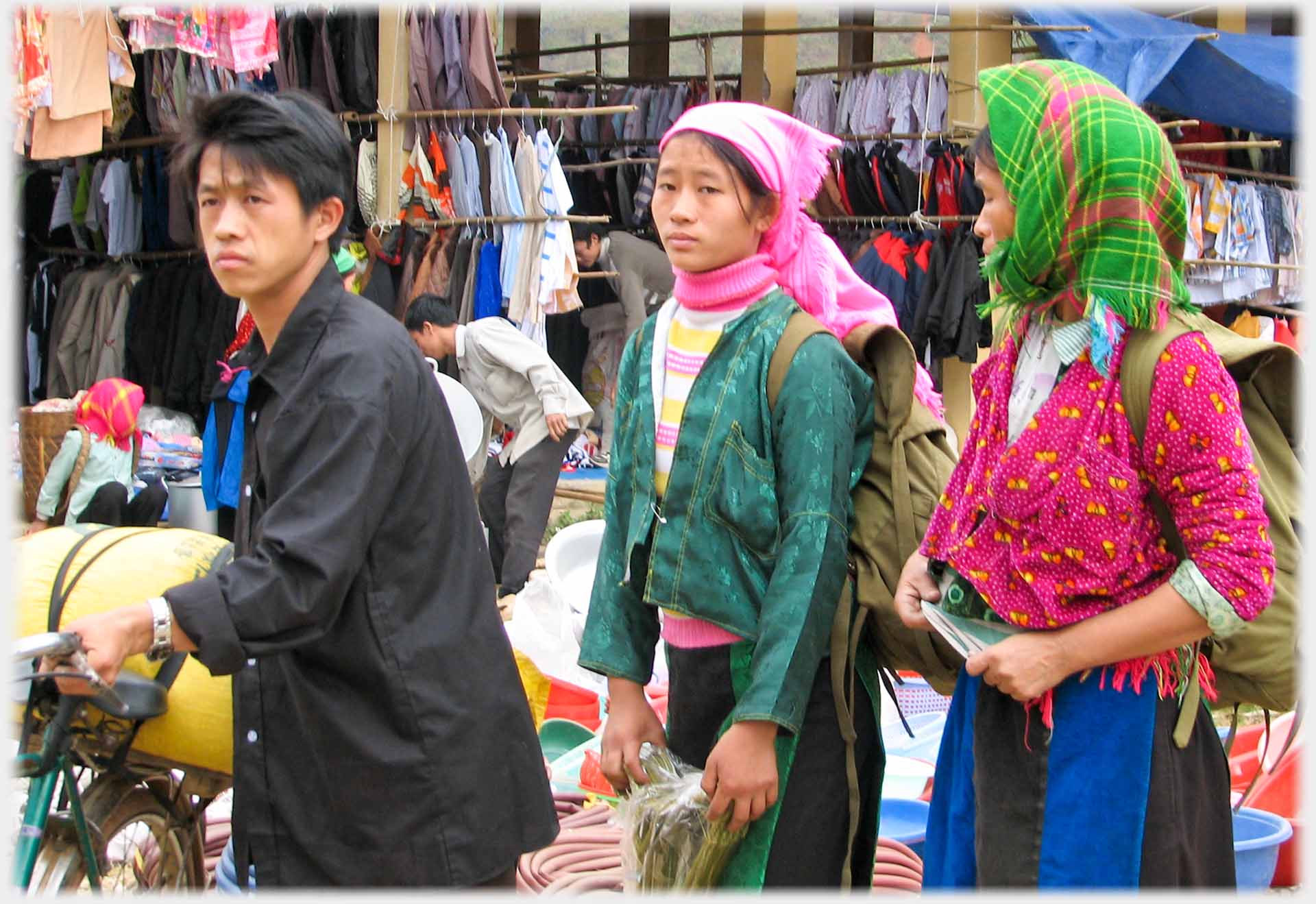 Man wheeling bicycle with load, two women behind.