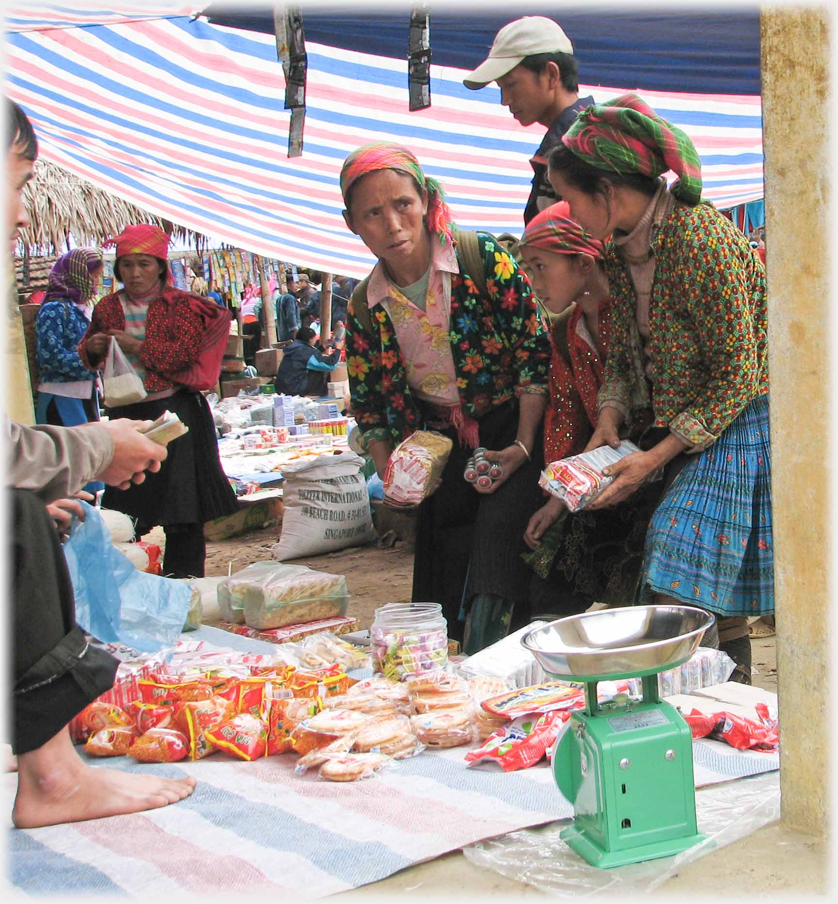 Two women and a girl at a stall, man holding money.