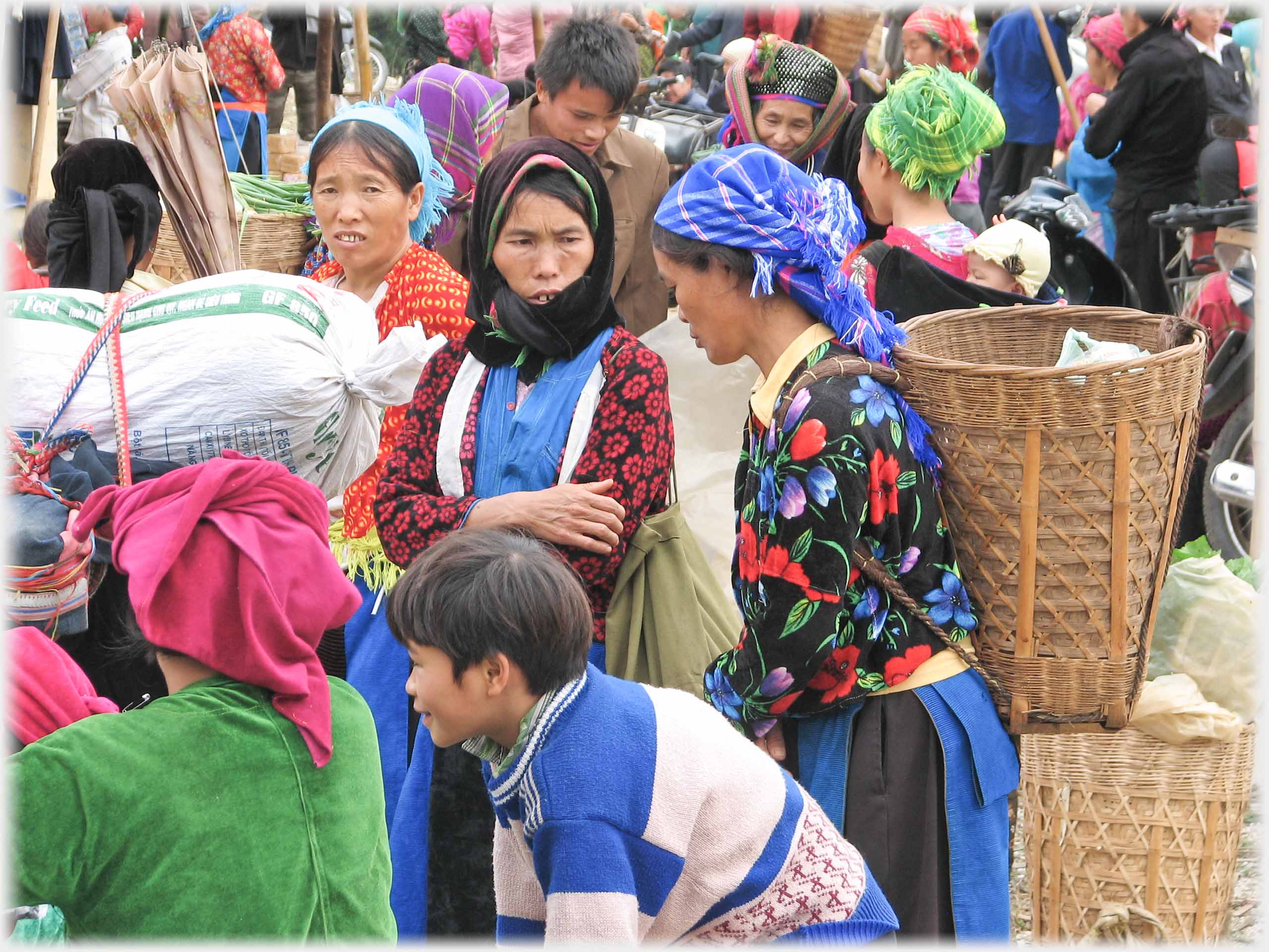 Three women, one with back-basket in crowd.