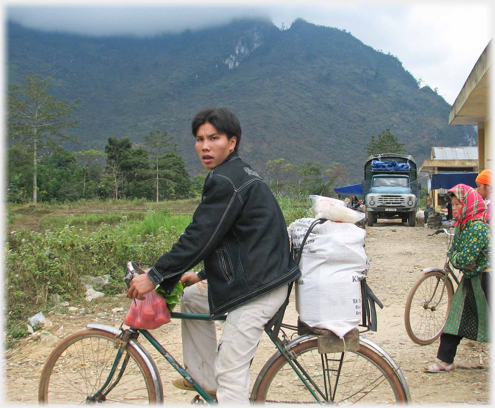 Man leaving market on bicycle with sack on back.