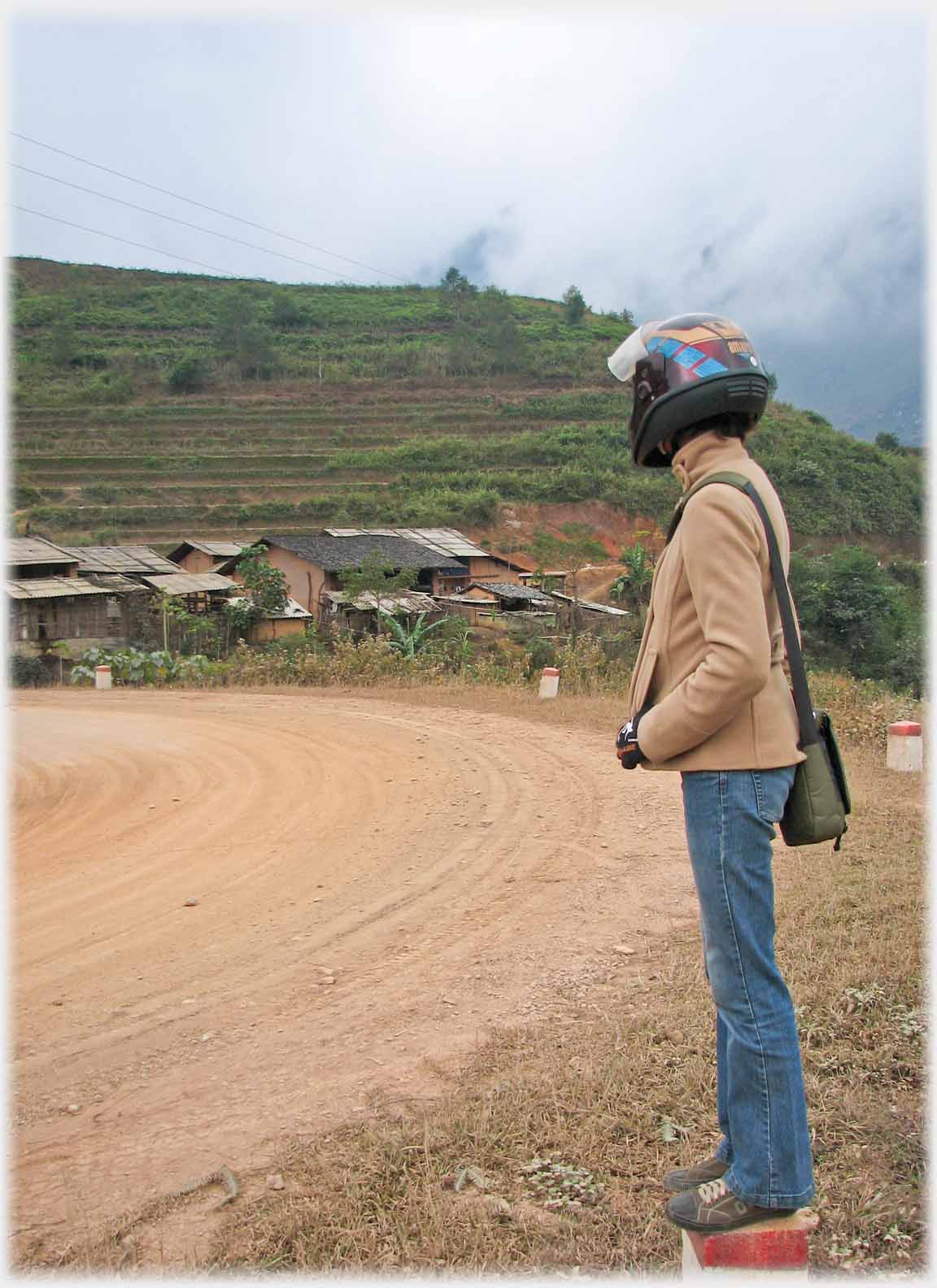 Helmeted figure standing on roadside concrete block.
