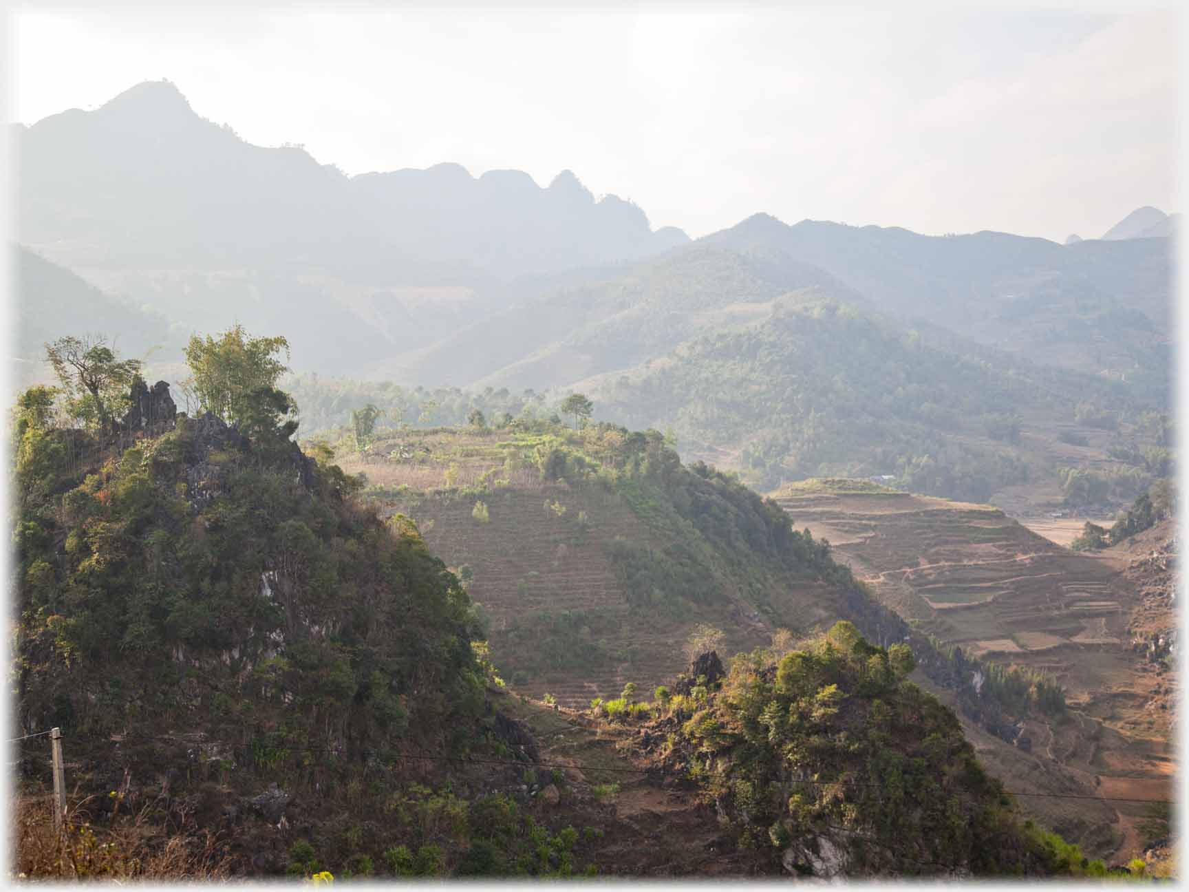 Hillocks with scrub and terracing, jagged hills in background.