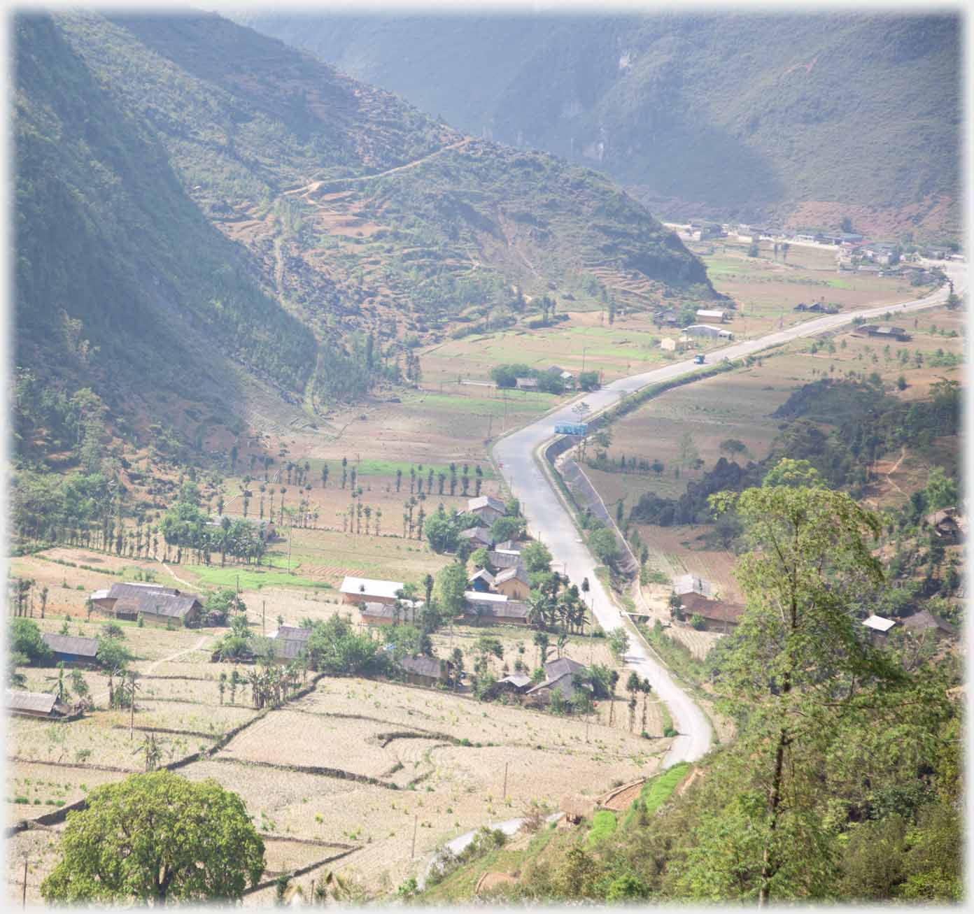 Flat bottomed valley with fields and houses beside road.