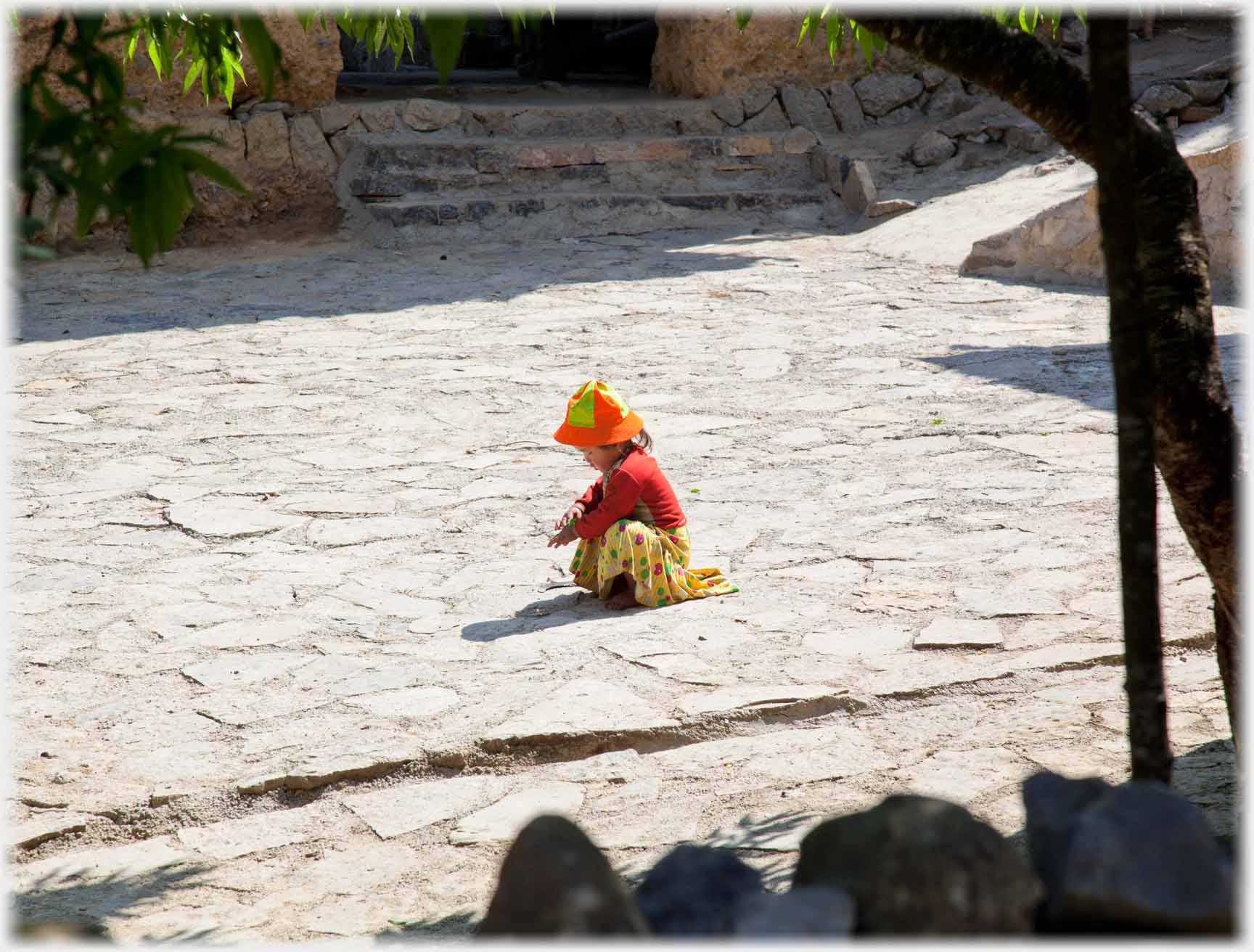 Small child in ara of paving in orange hat and cardigan.