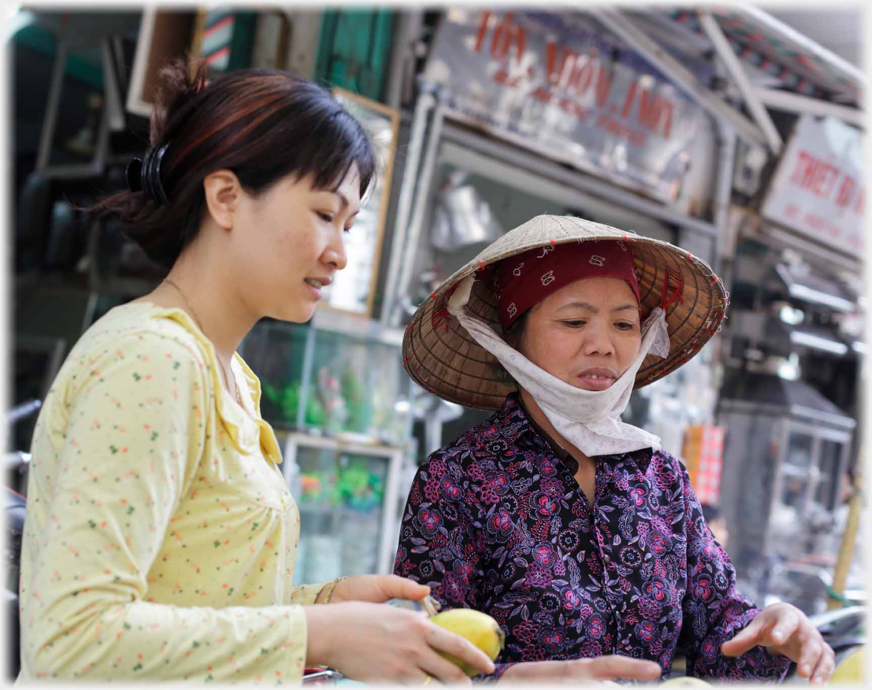 Woman in yellow top holding yellow fruit beside vendor.