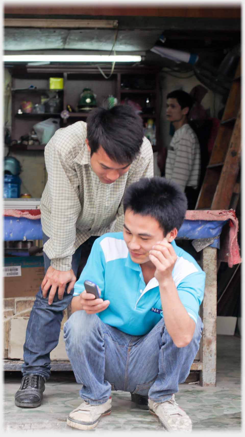 Man squatting with phone, another looks over his shoulder.