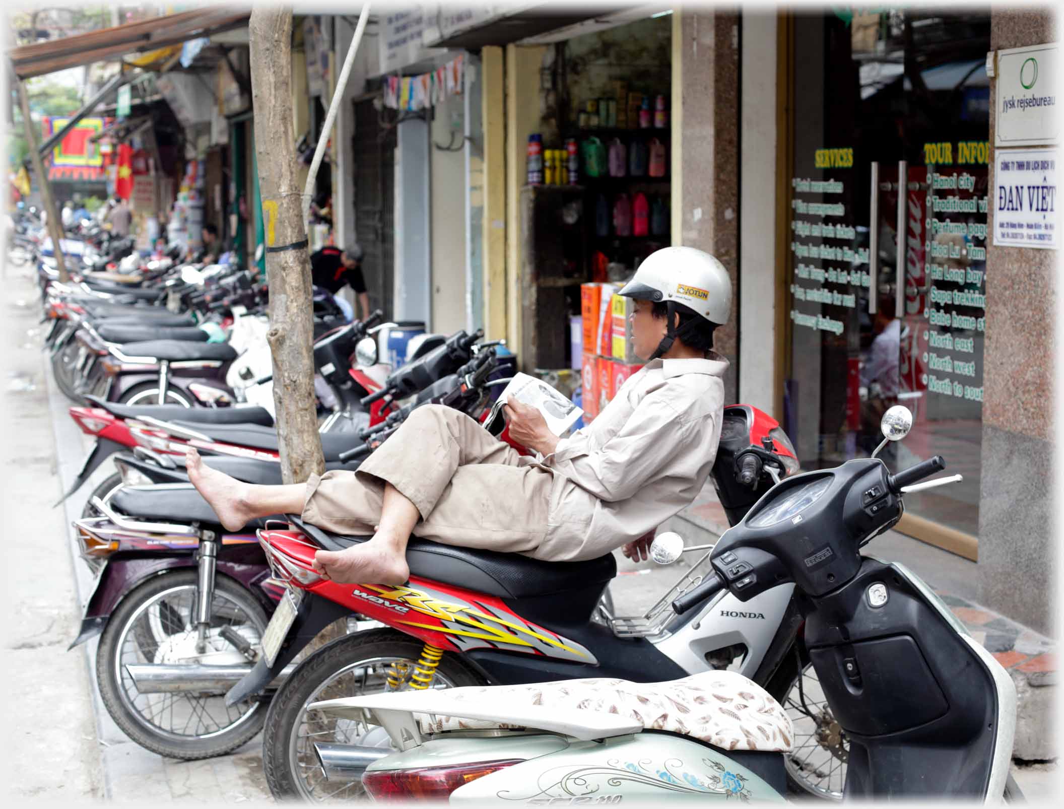Man reclining on motorbike parked in a long row of bikes.