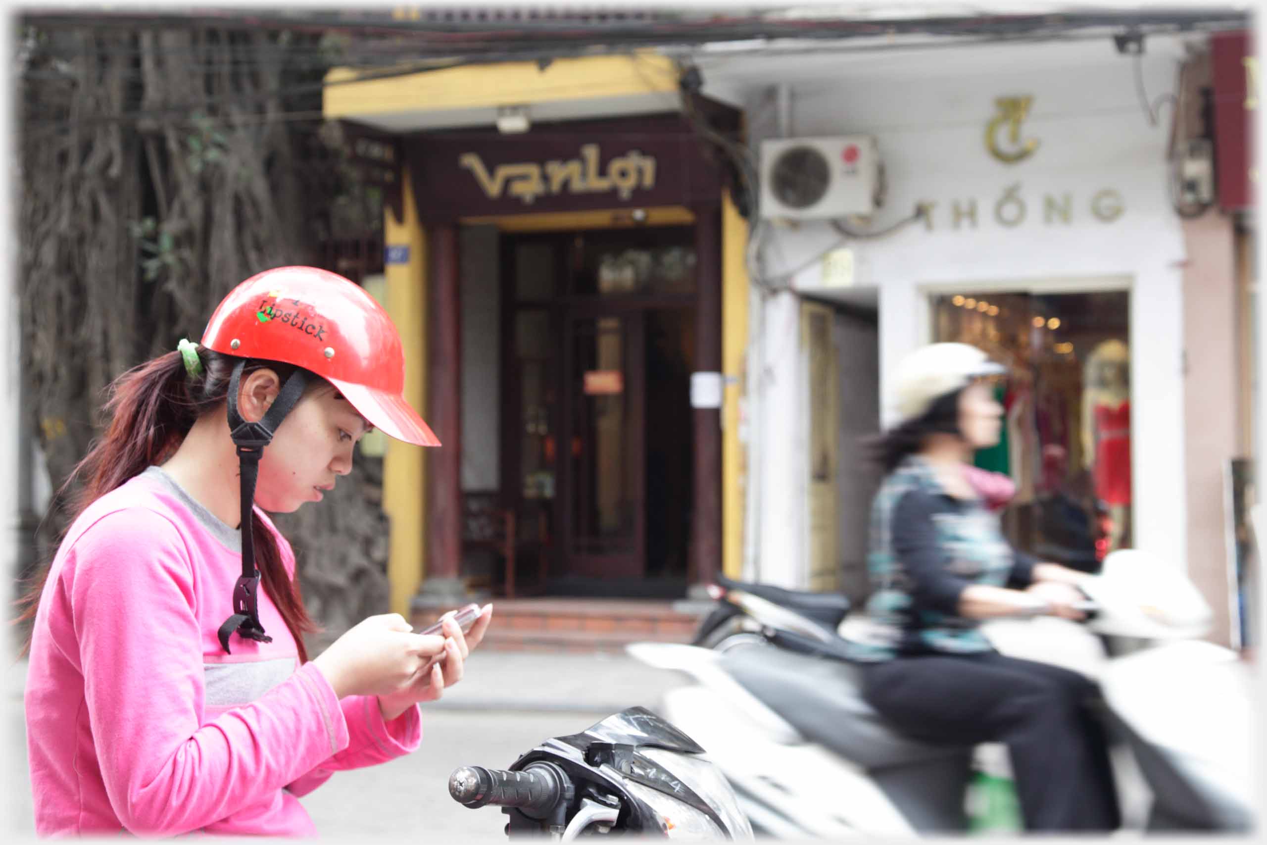 Woman in crash helmet texting, blurred image of passing woman.