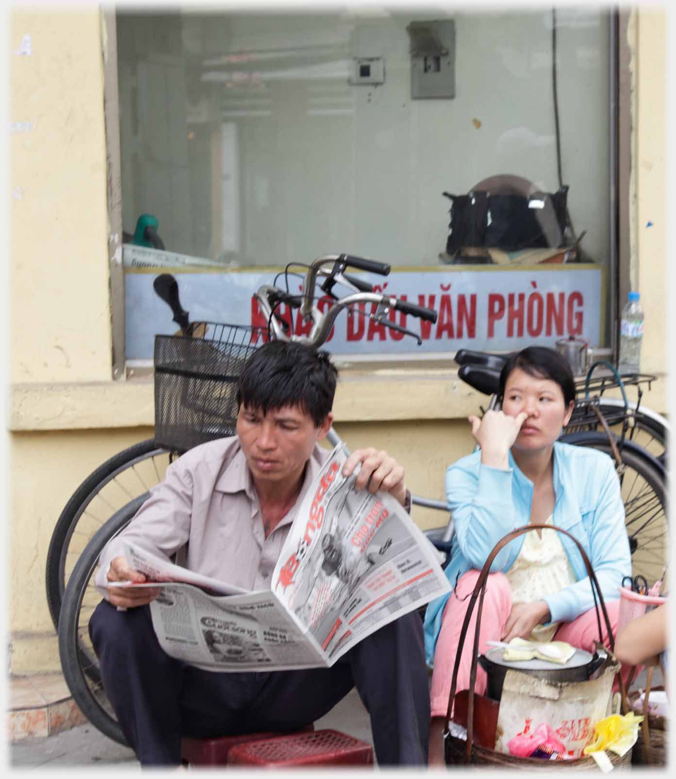 Man sitting reading newspaper, woman sitting behind him.