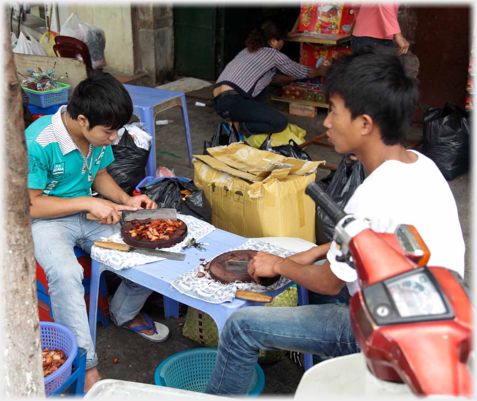 Two men sitting at caafe table cutting meat on blocks with cleavers.