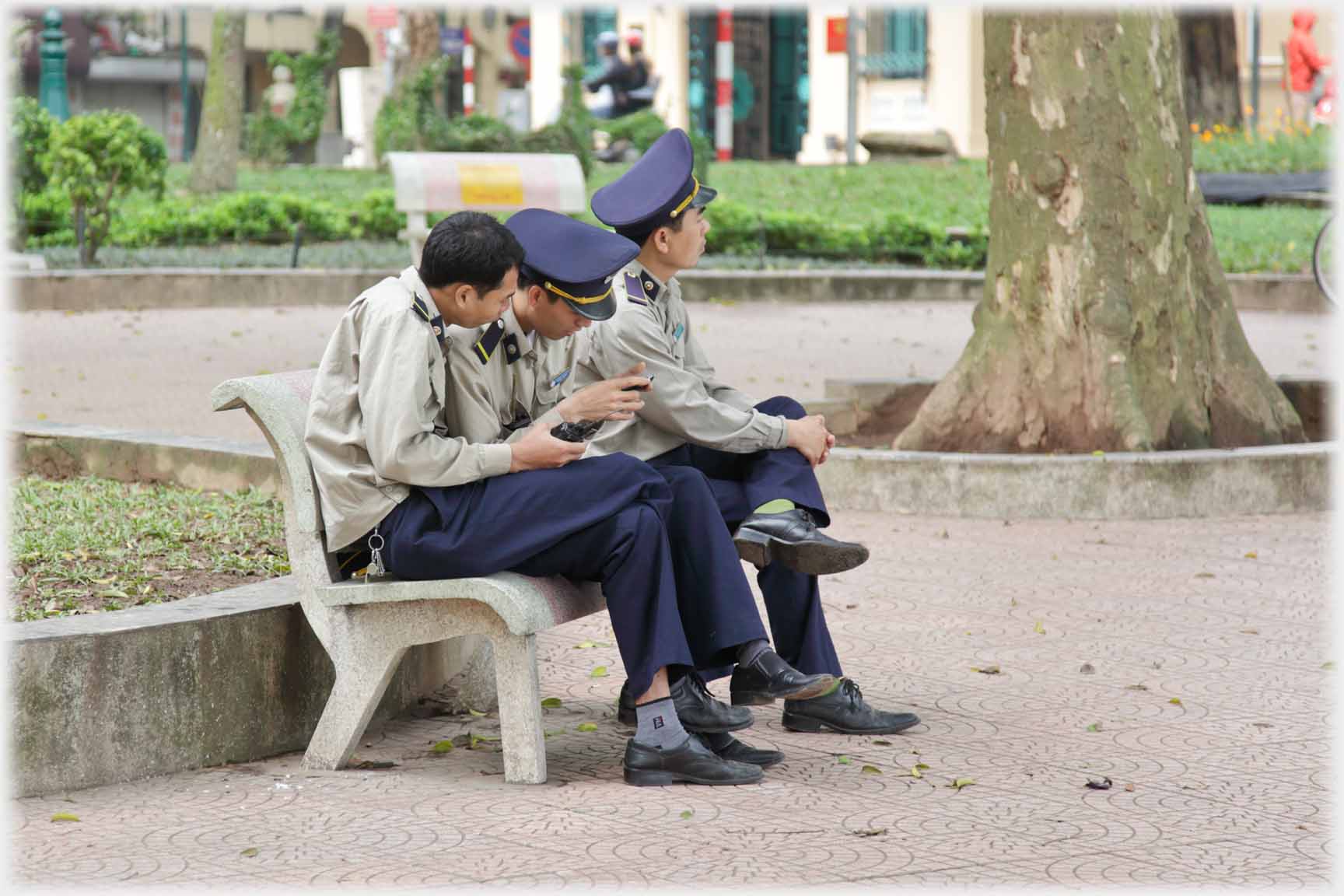 Three uniformed park security guards seated, two engrossed with phone.