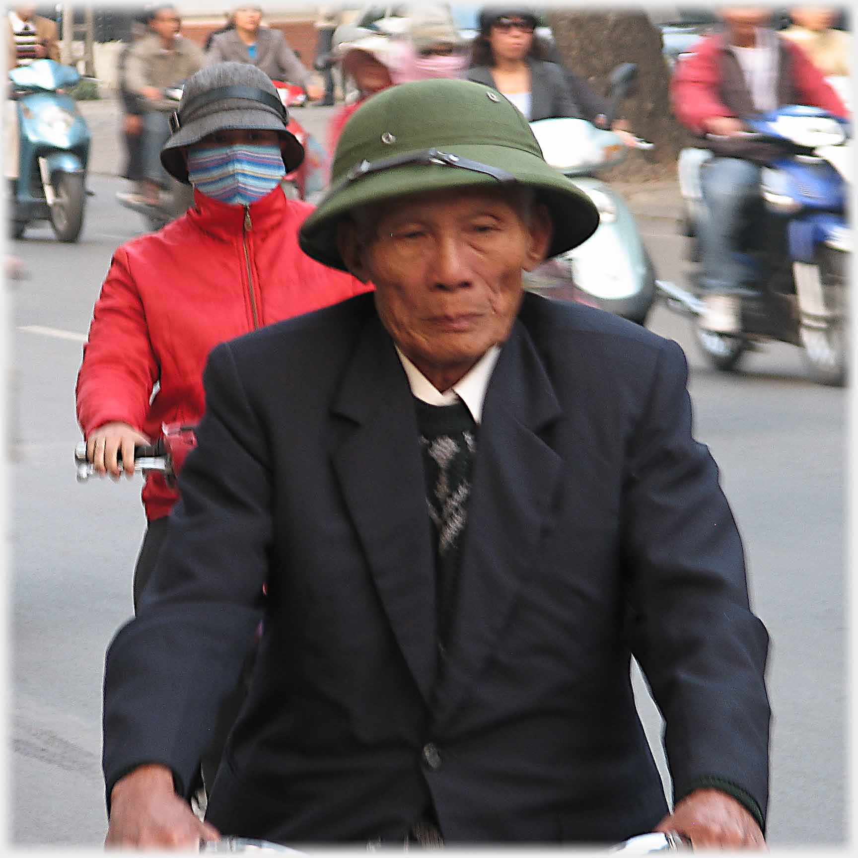 Older man in hat and jacket cycling thoughtfully.