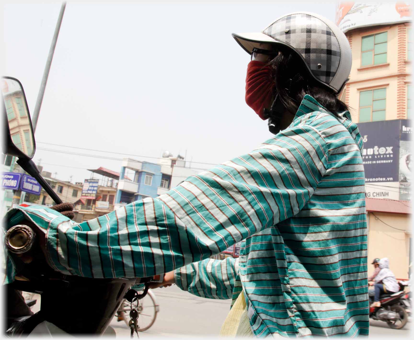 Woman on motorbike completely covered with helmet, glasses, mask and gown over her arms and hands.