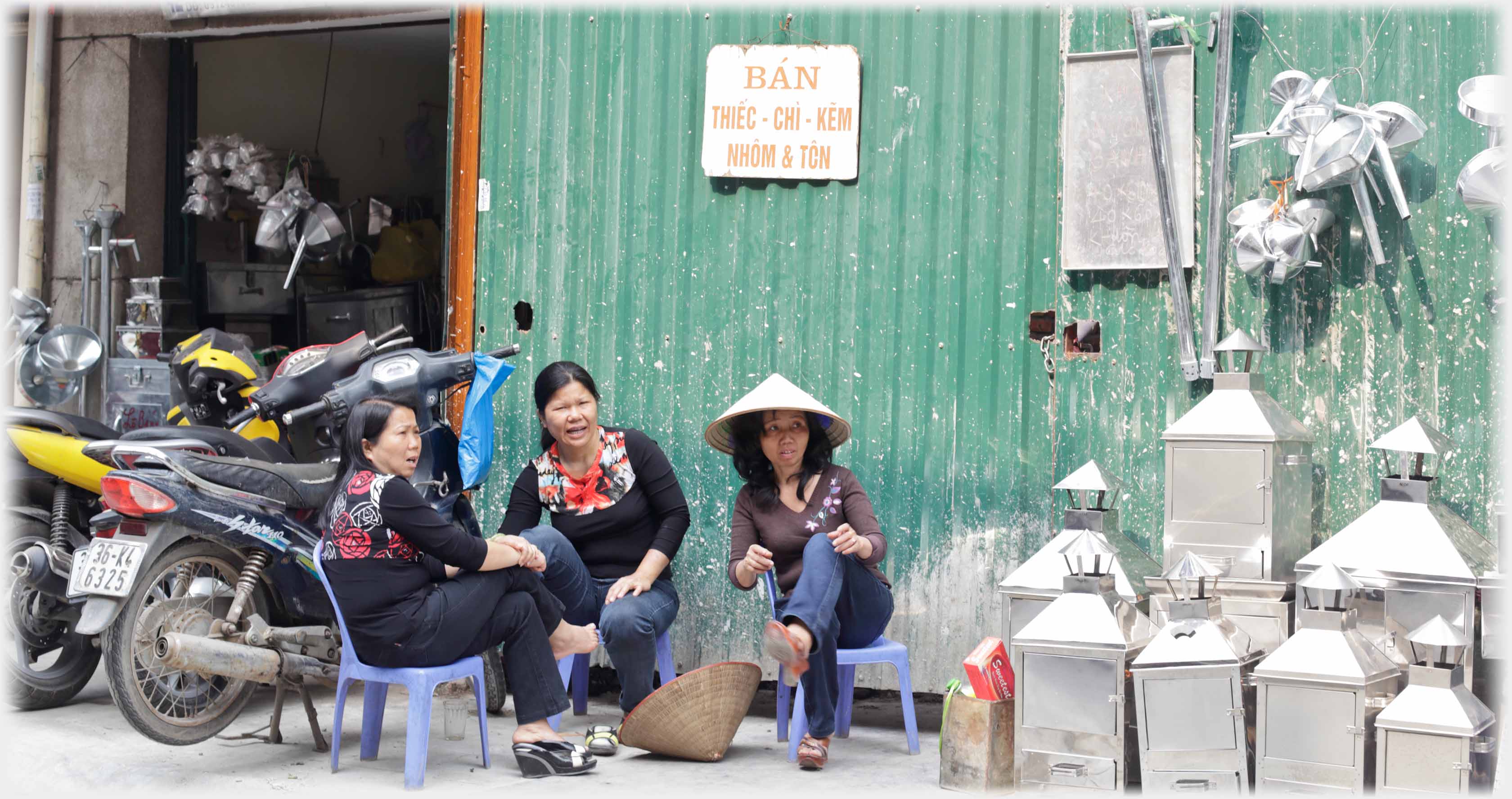 Group of three women sitting mouths open looking to the right. Notice on wall above, metal objects beside them.