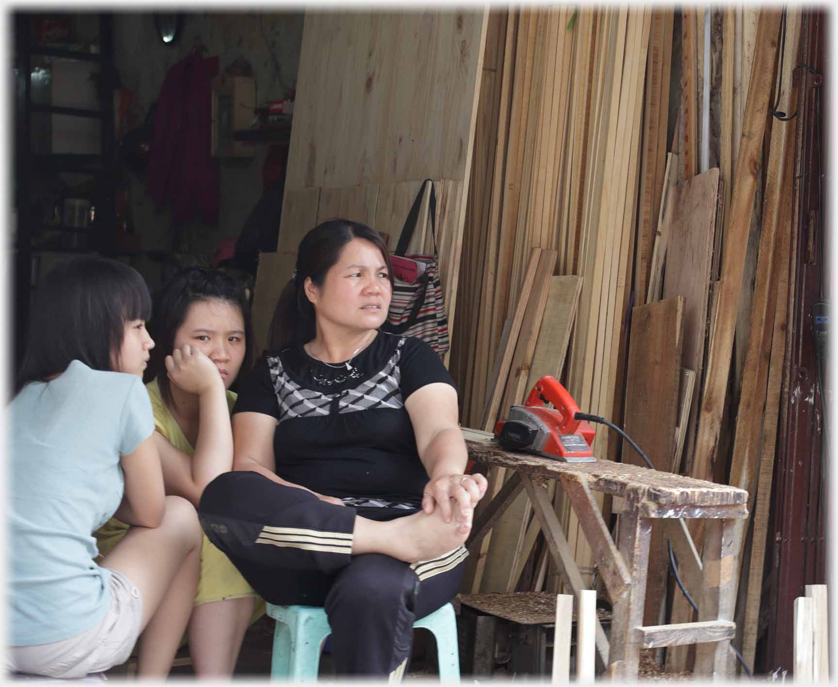 Three women by wood stacks with anxious faces.