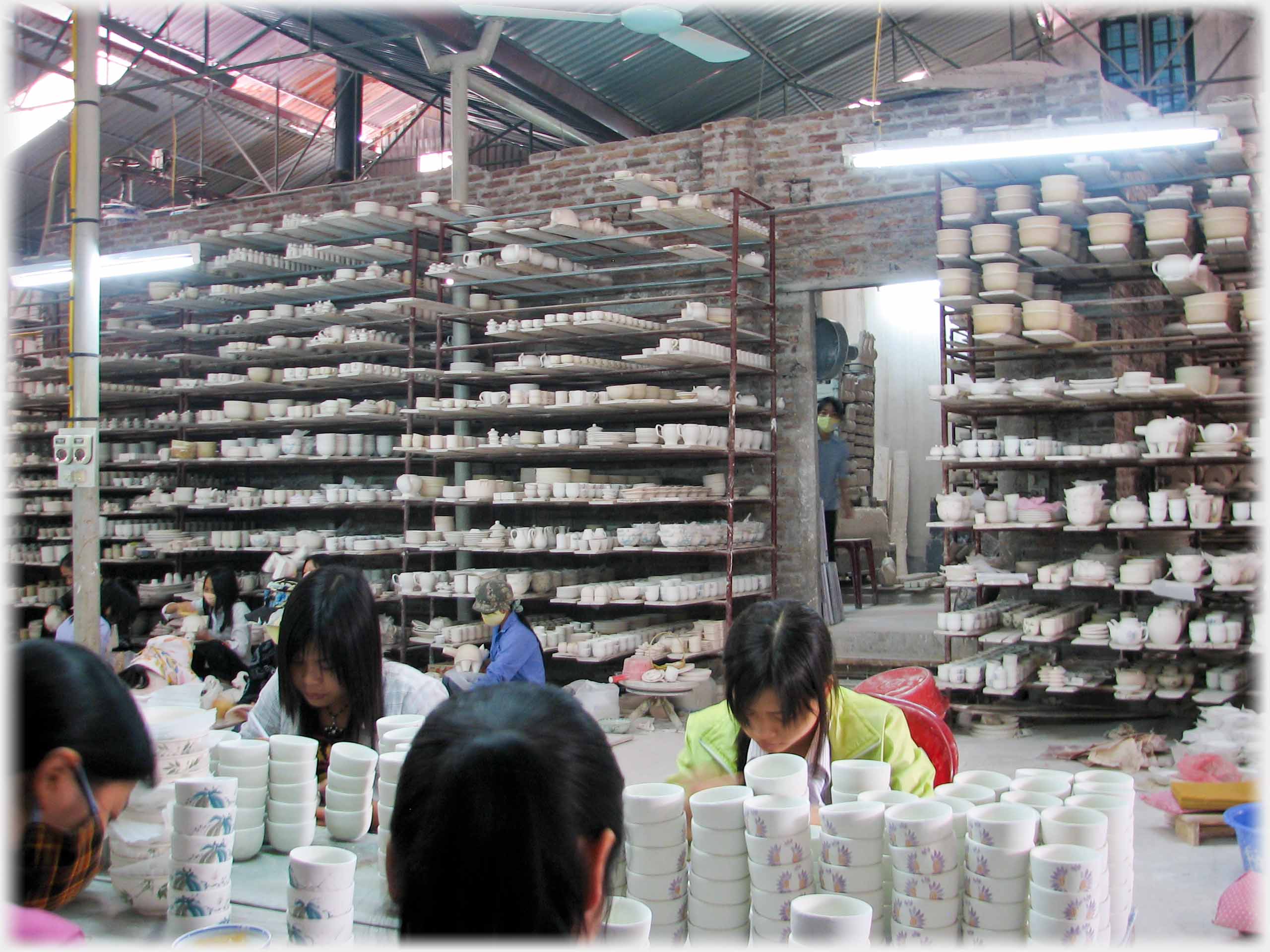 Warehouse with several workers painting pots, and high tiers of shelves behind.