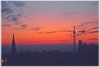 Sunset behind a crane and a spire.