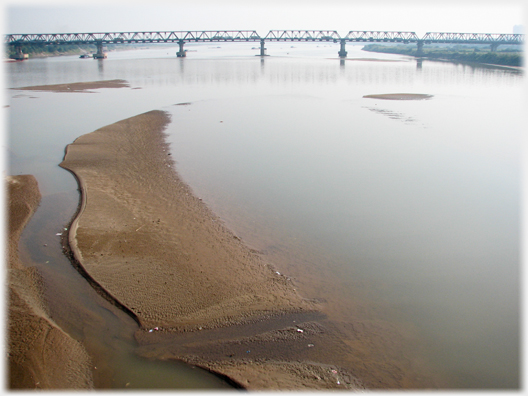 Sand-bank in river and bridge running across in distance.