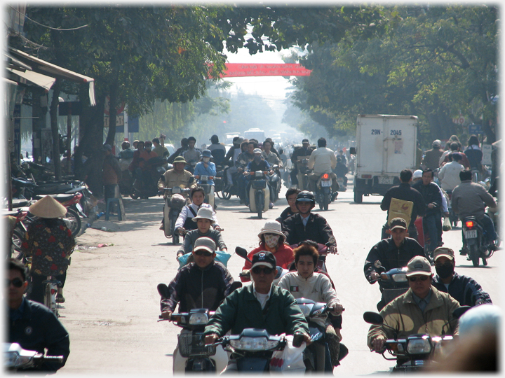 Sun behind motorcyclists on tree lined street.