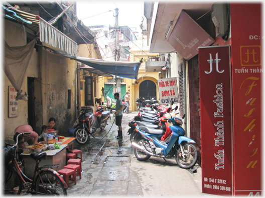 Lane with row of motorbikes and man hosing one.