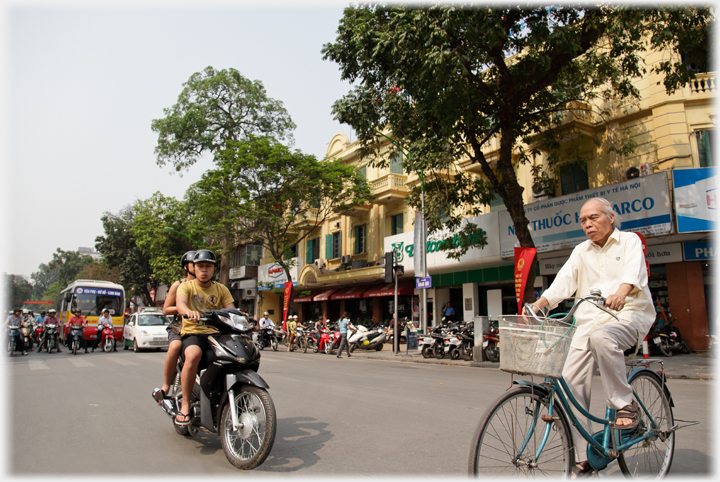 Elderly man cycling across big street with motorbike waiting for him.