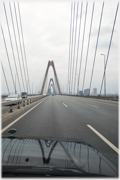 Arches of new suspension bridge reflected on bonnet of car.