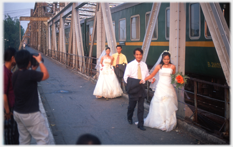 Two wedding couples being photographed on walkway beside train.