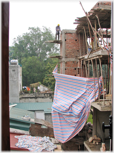 Building under construction with man standing on unfenced platform fifty feet up.