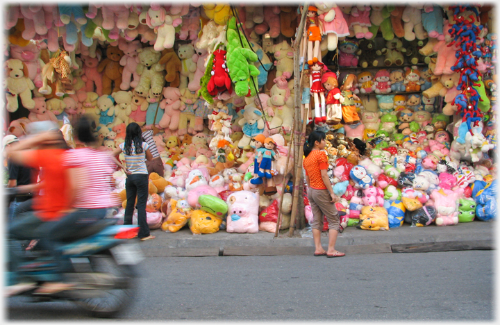 Two open fronted shops on the street, walls covered to the ceiling with stuffed toys, mostly bears.