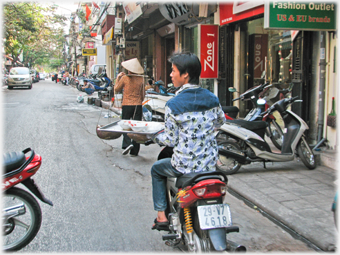 Man riding motorbike holding tray with bowls on his flat left hand - wiater style.