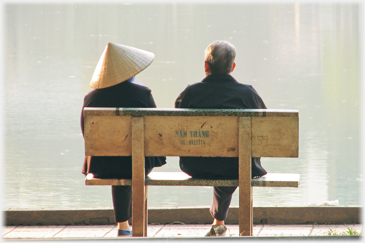 Two people sitting on seat by water.